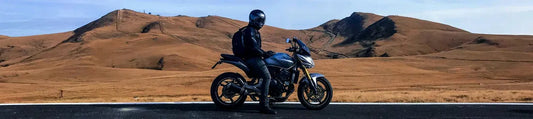 Motorcyclist stopped beside a scenic road with rolling hills, representing motorcycle GPS tracking and journey protection